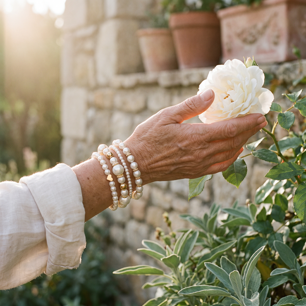 Woman wearing her pearl bracelet stack holding a white rose in the garden